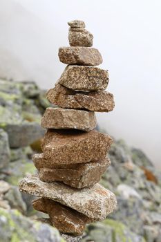 Close up balanced cairn or troll stoned pyramid, tourist memory sign or hiking path marking, built in foggy rocky mountains, low angle side view