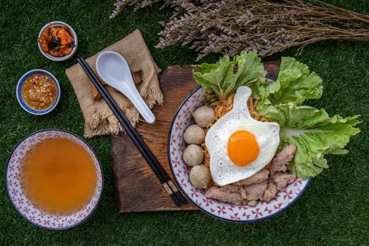 Boil egg noodles with pork ball, minced pork, fried egg, vegetables and soups in bowl and chopstick with spoon and timber background. Thai noodle soup.