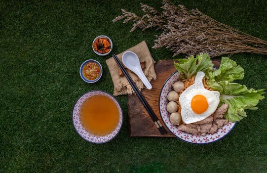 Boil egg noodles with pork ball, minced pork, fried egg, vegetables and soups in bowl and chopstick with spoon and timber background. Thai noodle soup.