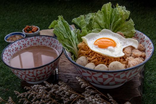 Boil egg noodles with pork ball, minced pork, fried egg, vegetables and soups in bowl and chopstick with spoon and timber background. Thai noodle soup.