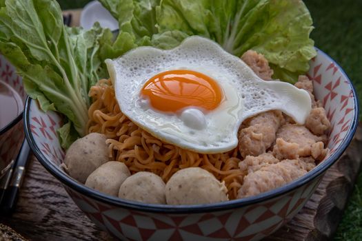Boil egg noodles with pork ball, minced pork, fried egg, vegetables and soups in bowl and chopstick with spoon and timber background. Thai noodle soup.
