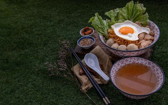 Boil egg noodles with pork ball, minced pork, fried egg, vegetables and soups in bowl and chopstick with spoon and timber background. Thai noodle soup.