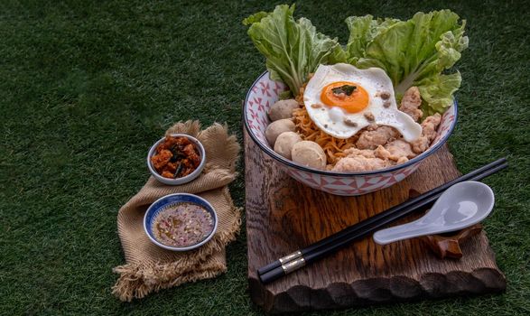 Egg noodles soup with pork ball, minced pork, fried egg, vegetables and soups in bowl and chopstick with spoon and timber background. Thai noodle soup.