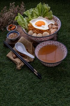 Boil egg noodles with pork ball, minced pork, fried egg, vegetables and soups in bowl and chopstick with spoon and timber background. Thai noodle soup.