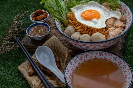 Boil egg noodles with pork ball, minced pork, fried egg, vegetables and soups in bowl and chopstick with spoon and timber background. Thai noodle soup.