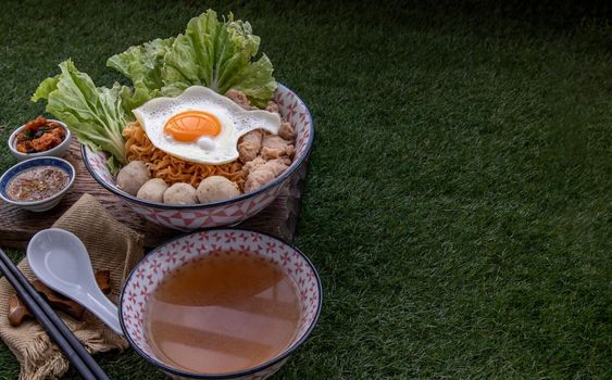 Boil egg noodles with pork ball, minced pork, fried egg, vegetables and soups in bowl and chopstick with spoon and timber background. Thai noodle soup.