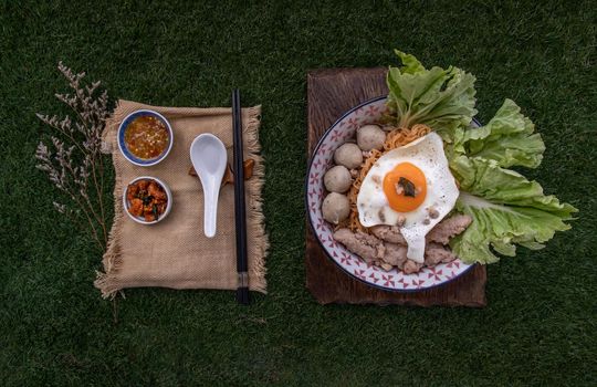 Egg noodles soup with pork ball, minced pork, fried egg, vegetables and soups in bowl and chopstick with spoon and timber background. Thai noodle soup.