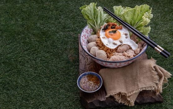 Egg noodles soup with pork ball, minced pork, fried egg, vegetables and soups in bowl and chopstick with spoon and timber background. Thai noodle soup.
