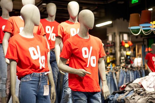 Percentage sign painted on a red t-shirt dressed on a mannequin stands in defocused store denoting big seasonal discounts