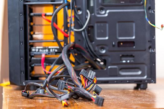bunch of computer power supply wires sticking out from opened black pc case - close-up with selective focus.