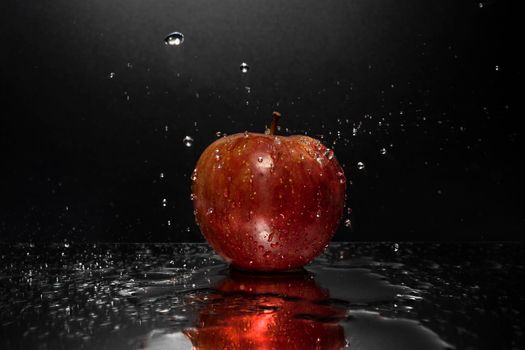 A red apple resting on a mirror with falling water drops