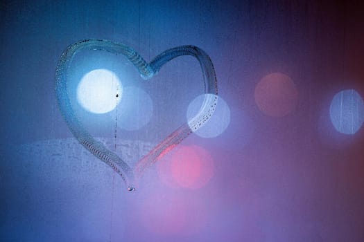 heart symbol hand drawn on wet night window glass in blue colors.