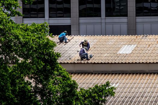 Bangkok, Thailand - 13 Jun 2020 : Three handyman workers repairing tiles on the damaged factory roof.