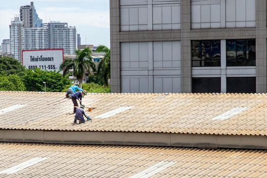 Bangkok, Thailand - 13 Jun 2020 : Two handyman workers repairing tiles on the damaged factory roof.