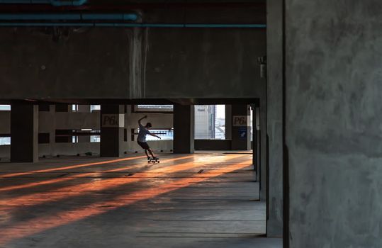 Bangkok, thailand - Mar 26, 2020 : A young man riding a skateboard in a parking lot at evening. The concept of modernity, youth and active lifestyle. No focus, specifically.