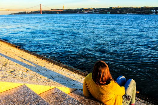 Girl sitting next to the riverbank at sunset in Lisbon, Portugal
