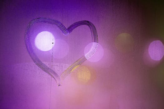 heart symbol hand drawn on wet night window glass in pink colors.