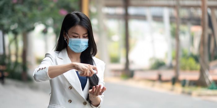 Portrait of businesswoman wearing mask sanitizing hands at post pandemic office, copy space