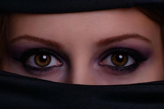 Close up portrait of a gorgeous female face with crystal and shiny eyes with beauty make up, wearing black scarf niqab hijab around her face. Burqa, hijab, niqab. Arabic, mysterious, authentic, mystic, beauty, fashion.