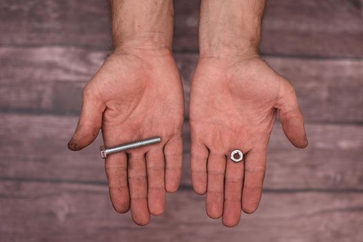 In the men's hands are a bolt and a nut. The man shows the fasteners. Dirty hands.