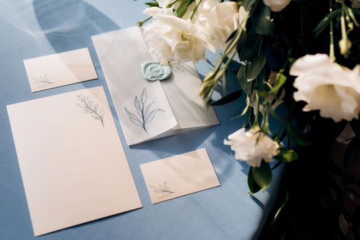 wedding invitation in a blue envelope on a table with green sprigs