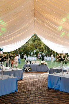 The presidium of the newlyweds in the banquet hall of the restaurant is decorated with candles and green plants, wisteria hangs from the ceiling