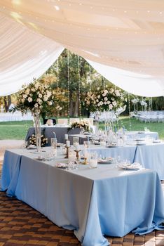 The presidium of the newlyweds in the banquet hall of the restaurant is decorated with candles and green plants, wisteria hangs from the ceiling