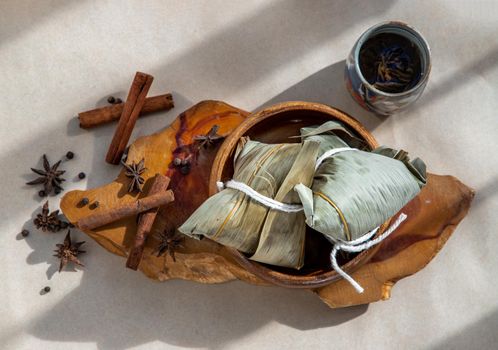 Chinese rice dumplings (Zongzi) shaped pyramidal wrapped by leaves ingredients on wooden plate. Famous asian tasty handmade food in dragon boat (duan wu) festival occasion.
