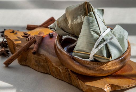 Chinese rice dumplings (Zongzi) shaped pyramidal wrapped by leaves ingredients on wooden plate. Famous asian tasty handmade food in dragon boat (duan wu) festival occasion.