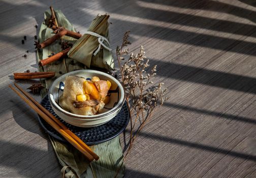 Chinese rice dumplings (Zongzi) shaped pyramidal wrapped by leaves ingredients on bowl chinese style and chopsticks. Famous asian tasty handmade food in dragon boat (duan wu) festival occasion.