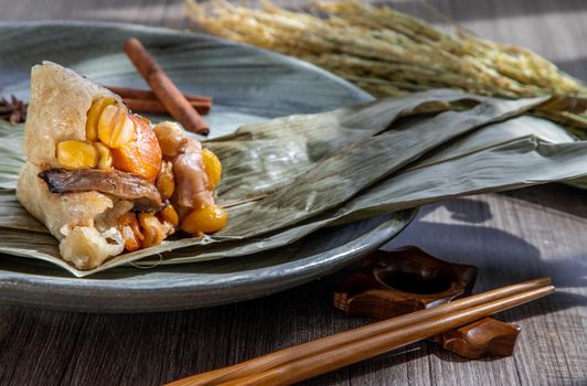 Chinese rice dumpling (Zongzi) shaped pyramidal wrapped by leaves ingredients on dried banana leaf. Famous asian tasty handmade food in dragon boat (duan wu) festival occasion.