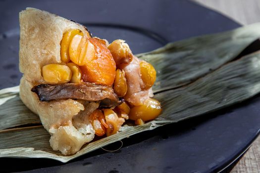 Chinese rice dumpling (Zongzi) shaped pyramidal wrapped by leaves ingredients on dried banana leaf. Famous asian tasty handmade food in dragon boat (duan wu) festival occasion.