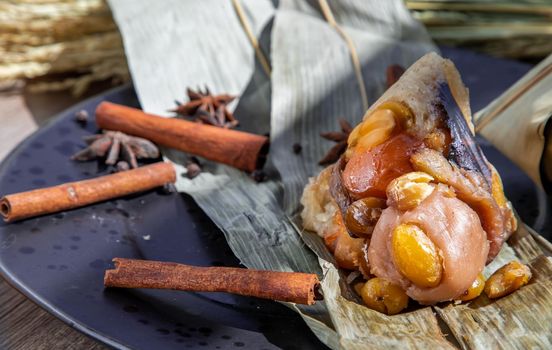 Chinese rice dumpling (Zongzi) shaped pyramidal wrapped by leaves ingredients on dried banana leaf. Famous asian tasty handmade food in dragon boat (duan wu) festival occasion.