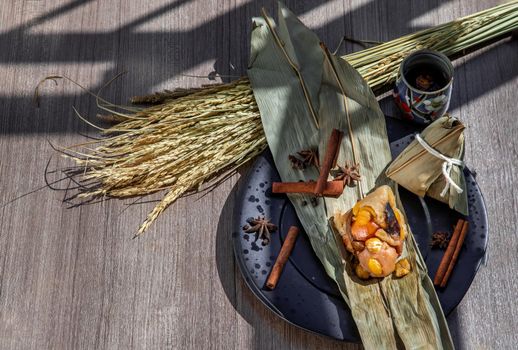 Chinese rice dumpling (Zongzi) shaped pyramidal wrapped by leaves ingredients on dried banana leaf Served with chinese tea. Famous asian tasty handmade food in dragon boat (duan wu) festival occasion.