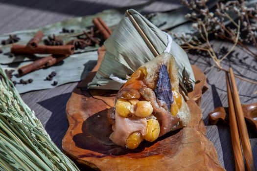 Chinese rice dumpling (Zongzi) shaped pyramidal wrapped by leaves ingredients on wooden plate and chopsticks. Famous asian tasty handmade food in dragon boat (duan wu) festival occasion.