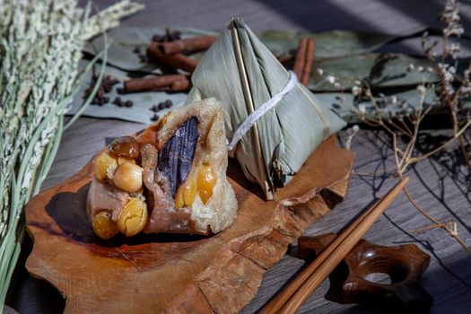 Chinese rice dumpling (Zongzi) shaped pyramidal wrapped by leaves ingredients on wooden plate and chopsticks. Famous asian tasty handmade food in dragon boat (duan wu) festival occasion.