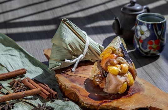 Chinese rice dumpling (Zongzi) shaped pyramidal wrapped by leaves ingredients on wooden plate Served with chinese tea and chopsticks. Famous asian tasty handmade food in dragon boat (duan wu) festival occasion.