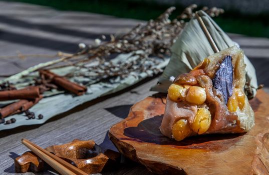 Chinese rice dumpling (Zongzi) shaped pyramidal wrapped by leaves ingredients on wooden plate and chopsticks. Famous asian tasty handmade food in dragon boat (duan wu) festival occasion.