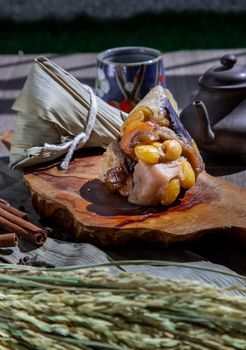 Chinese rice dumpling (Zongzi) shaped pyramidal wrapped by leaves ingredients on wooden plate Served with chinese tea. Famous asian tasty handmade food in dragon boat (duan wu) festival occasion.