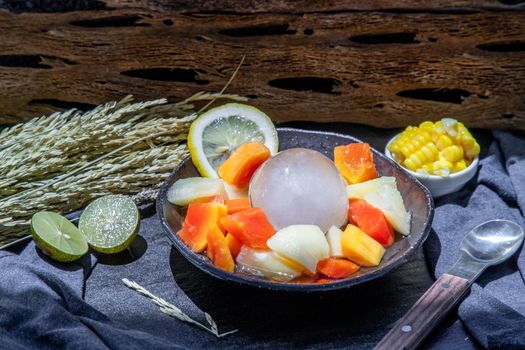 Tropical fresh fruit salad served with corn on black ceramic bowl in dark background.  Selective focus.
