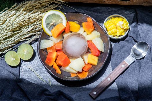 Tropical fresh fruit salad served with corn on black ceramic bowl in dark background.  Selective focus.