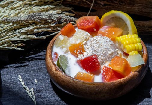 Tropical fresh fruit salad with milk and oatmeal on wooden bowl in dark background. Sweet healthy breakfast, Healthy vegan meal, Selective focus.