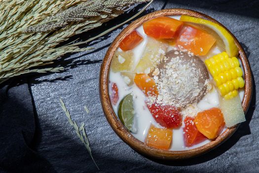 Tropical fresh fruit salad with milk and oatmeal on wooden bowl in dark background. Sweet healthy breakfast, Healthy vegan meal, Selective focus.