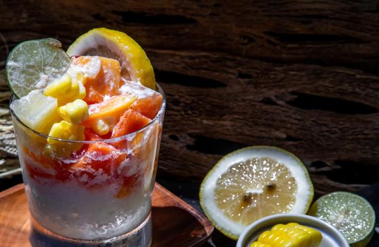 Tropical fresh fruit salad with milk and oatmeal in a glass cup served with corn on dark background. Sweet healthy breakfast, Healthy vegan meal. Selective focus.