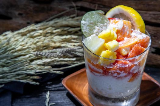 Tropical fresh fruit salad with milk and oatmeal  in a glass cup on dark background. Sweet healthy breakfast, Healthy vegan meal. Selective focus.
