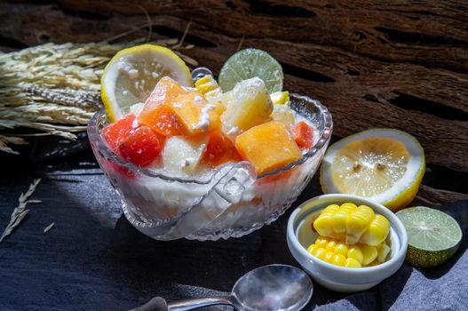 Tropical fresh fruit salad with milk and oatmeal in a glass bowl served with corn on dark background. Sweet healthy breakfast, Healthy vegan meal. Selective focus.