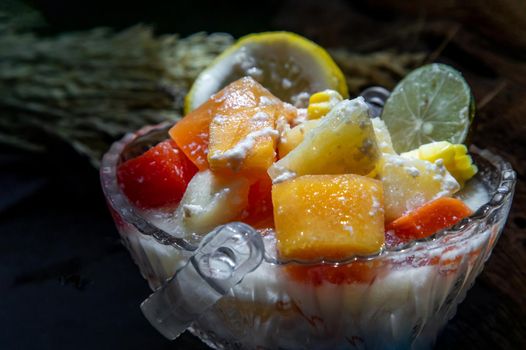 Tropical fresh fruit salad with milk and oatmeal in a glass bowl on dark background. Sweet healthy breakfast, Healthy vegan meal. Selective focus.