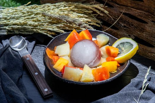 Tropical fresh fruit salad served with corn on black ceramic bowl in dark background.  Selective focus.