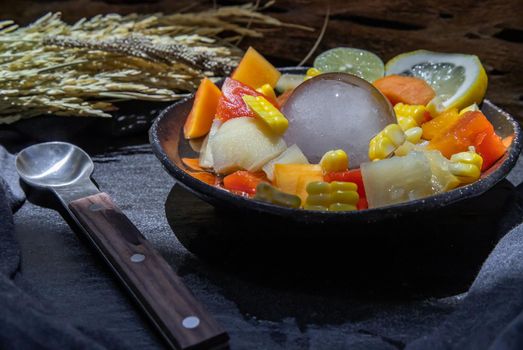 Tropical fresh fruit salad served with corn on black ceramic bowl in dark background.  Selective focus.