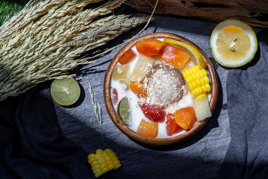 Tropical fresh fruit salad with milk and oatmeal on wooden bowl in dark background. Sweet healthy breakfast, Healthy vegan meal, Selective focus.